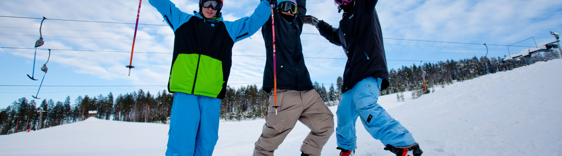 Tre personer i backen som sträcker armarna upp i luften. Har på sig slalomskidor, hjälmar och håller stavar i händerna.