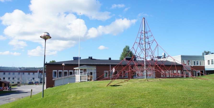 Sommarbild tagen på skolgården vid mellanstadiet med klätternät, grön gräsmatta och byggnader.