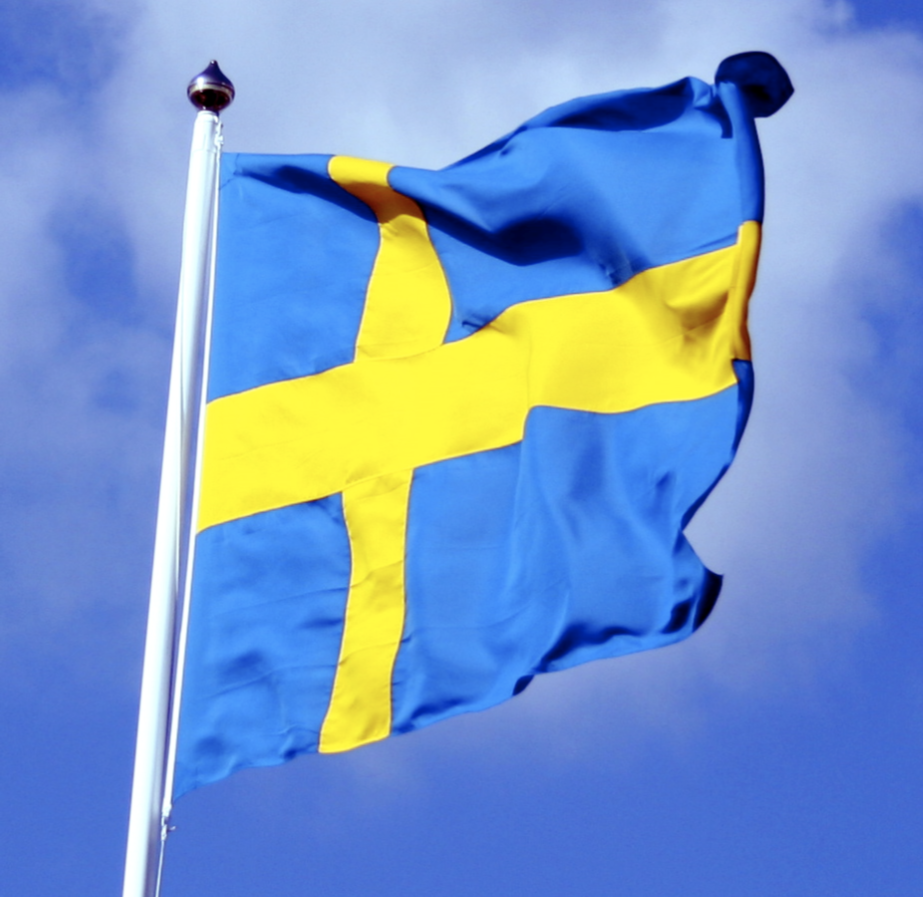 Svenska flaggans om sitter på en vit flaggstång med blå himmel i bakgrunden.