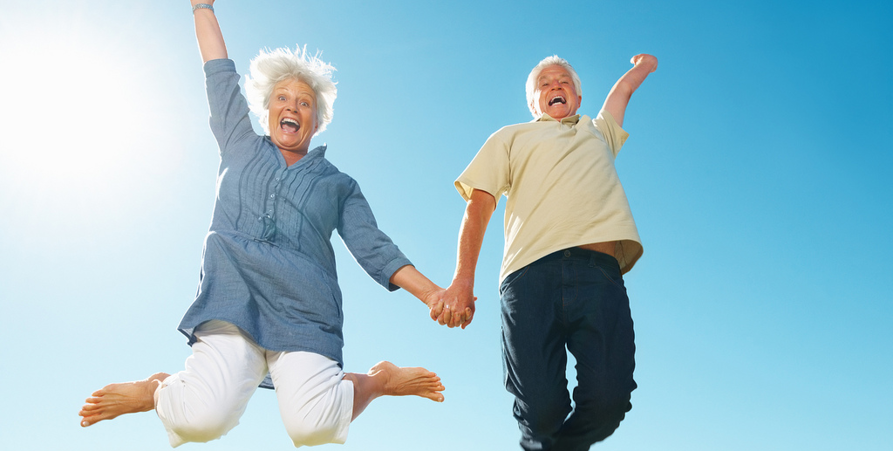 Två glada personer som hoppar upp, hand i hand, mot en solig blå himmel. 