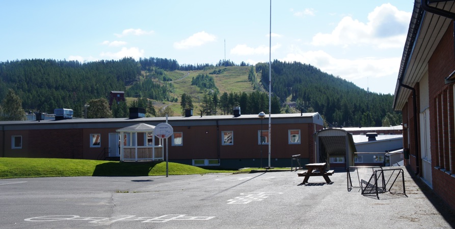 Sommarbild tagen vid skolgården på mellanstadiet med byggnader och Tjamstanberget i bakgrunden.