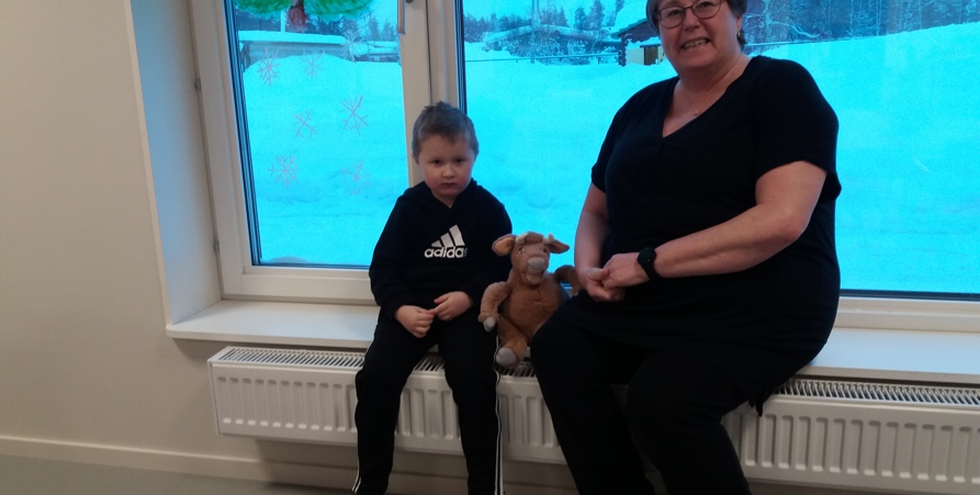 Förskolelärare som sitter vid ett fönster med en pojke och ett gosedjur.
