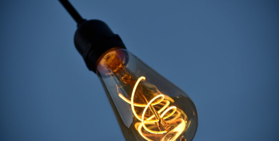 En glödlampa som lyser framför en blå bakgrund.