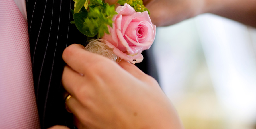Närbild på brudgum där bruden sätter en rosa ros på kavajen.
