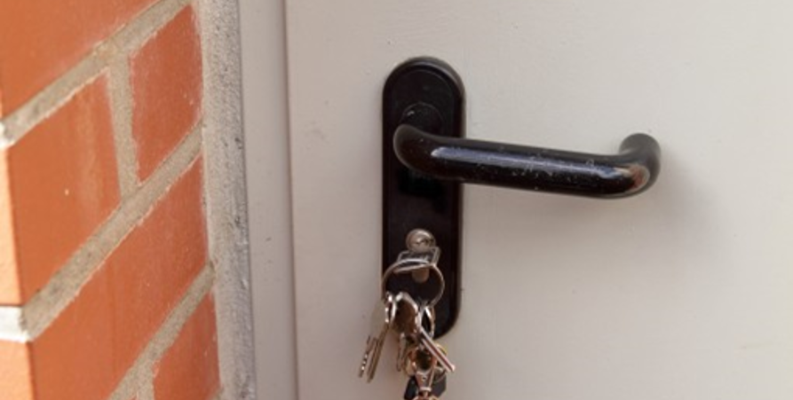Vit ytterdörr med svart handtag, där nyckelknippan sitter i dörrlåset.