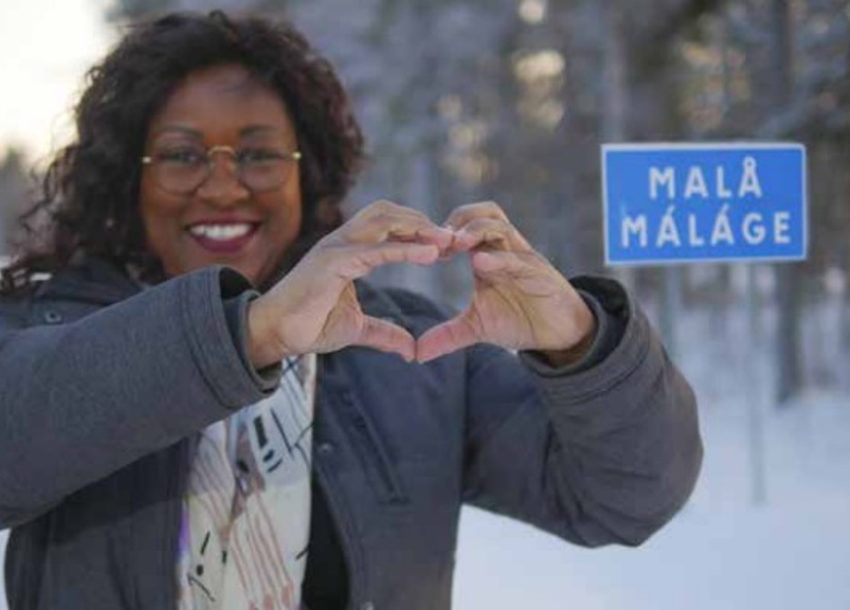 Kvinna formar händerna till ett hjärta framför Malå skylten