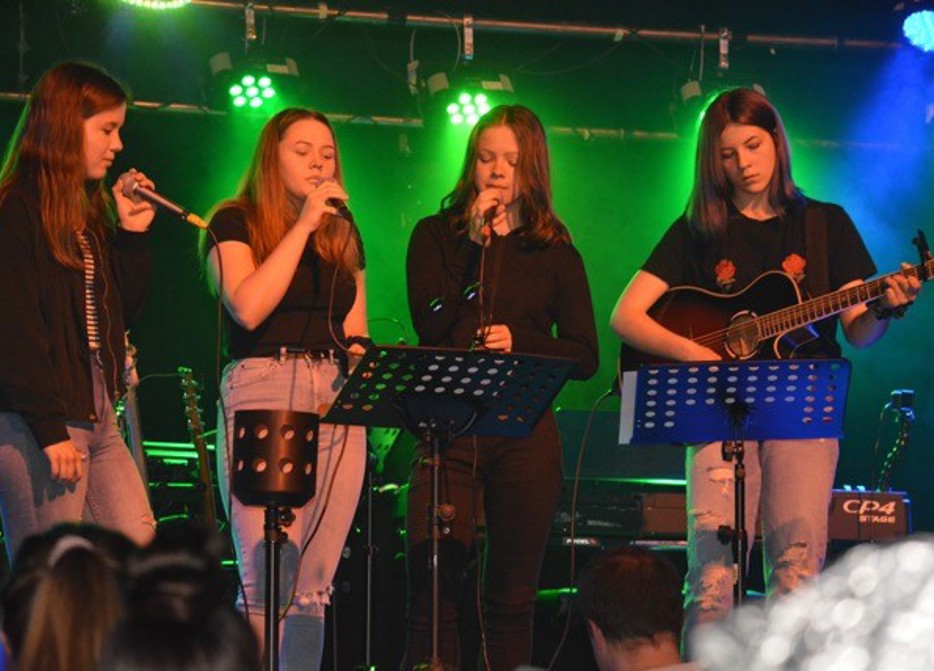 Fyra tjejer som spelar och sjunger på en scen.
