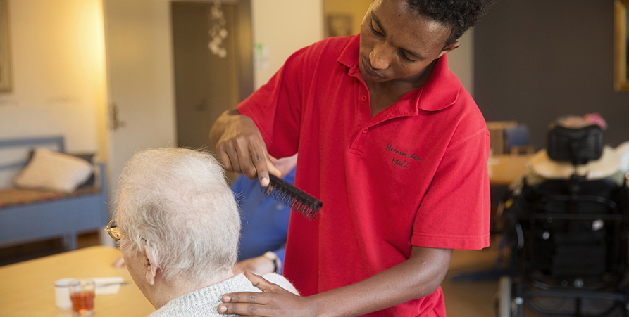 Manlig skötare inom äldreomsorg som kammar håret på en kvinna.