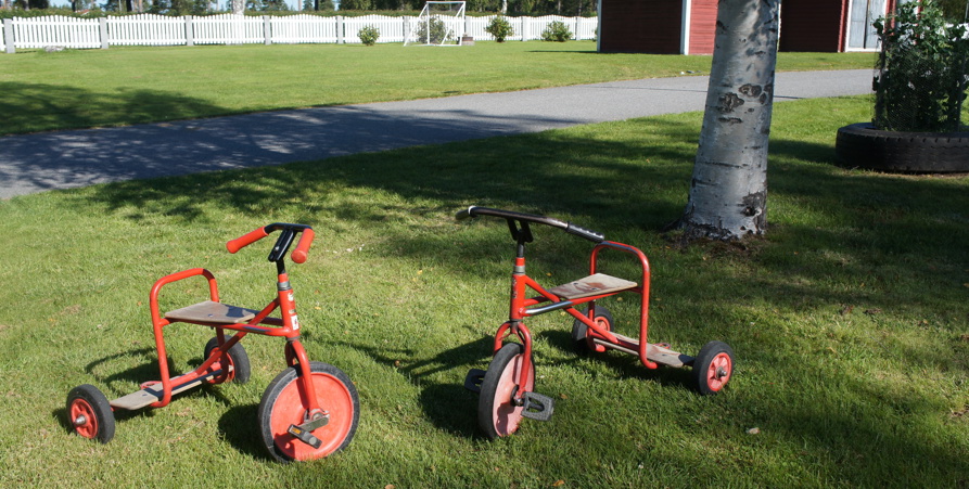 2 stycken röda trehjulingar som står vid varandra på gräset.