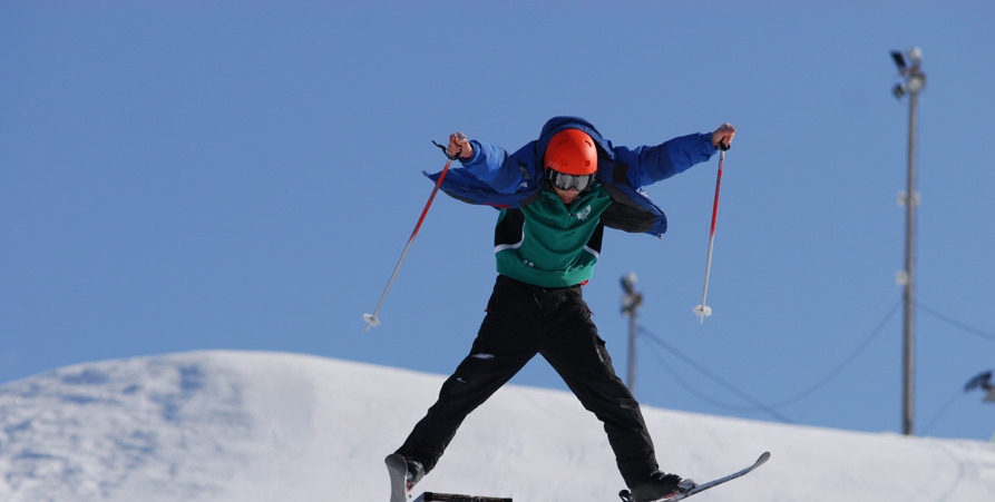 Pojke som hoppar med sina slalomskidor i Tjamstanbackarna. Himlen är klarblå.