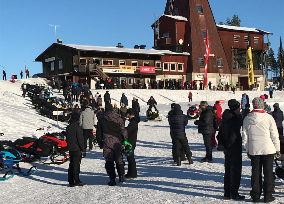 Skoterns dag 2020 som arrangerades i Tjamstanbackarna. Snö, människor och skotrar vid Lavenhuset. Strålande sol och blå himmel.