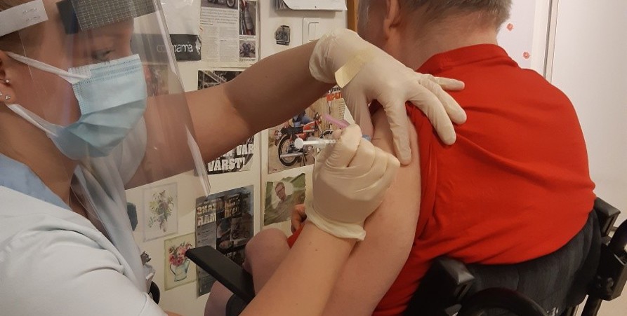 Sjuksköterska med tar vaccination på äldre man i rullstol.
