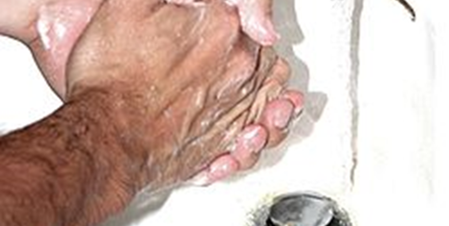 Närbild på när någon tvättar händerna under rinnande vatten, med texten: uppdaterad information om Coronaviruset, Covid-19.