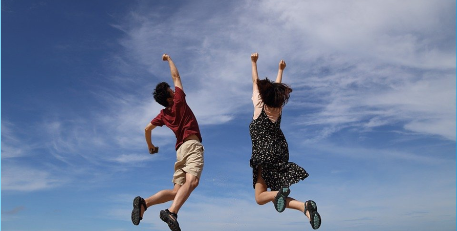 En kvinna och en man som hoppar upp mot klarblå himmel med uppsträckta armar.