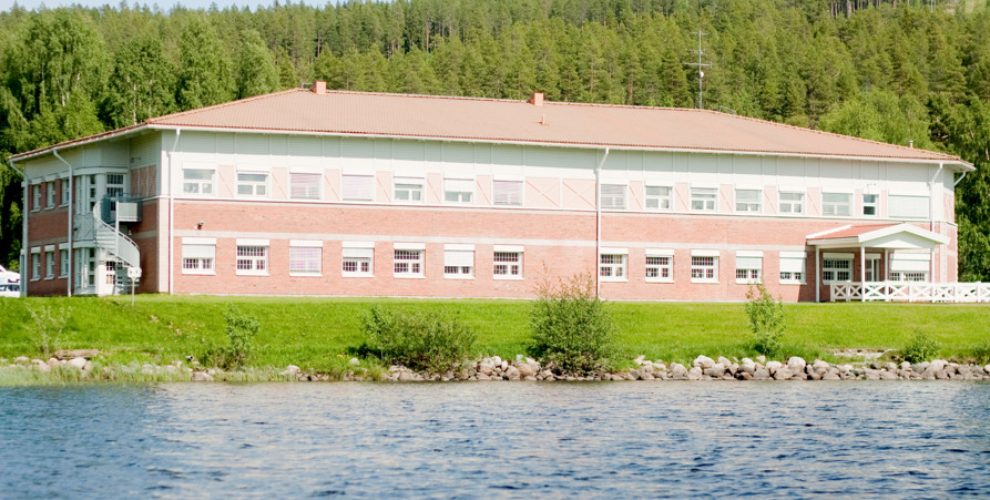 Bild på kommunhusets baksida med huset i rött tegel samt gräsmatta och Malån.