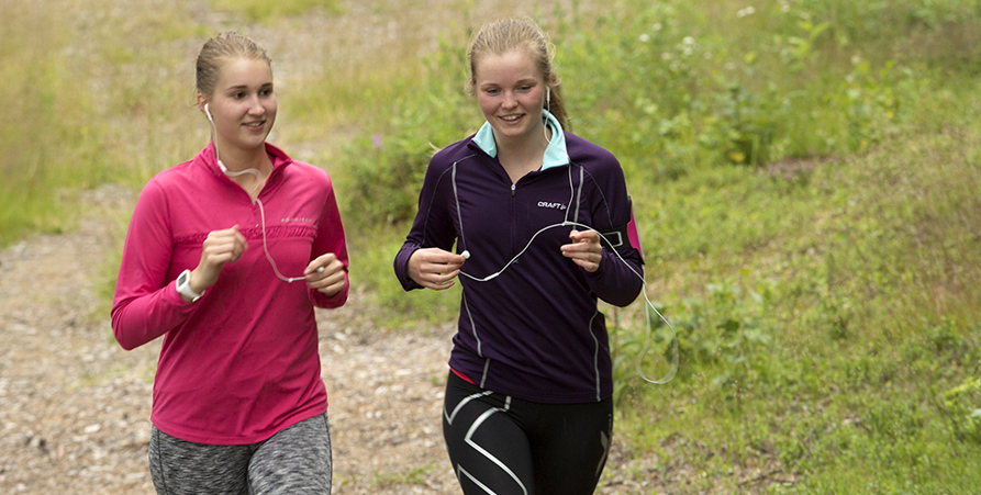 Två kvinnor som joggar bredvid varandra i motionsspåret. Se ser glada ut.