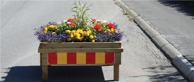 En blomlåda med blommor i och reflexer utanpå står på gatan 
